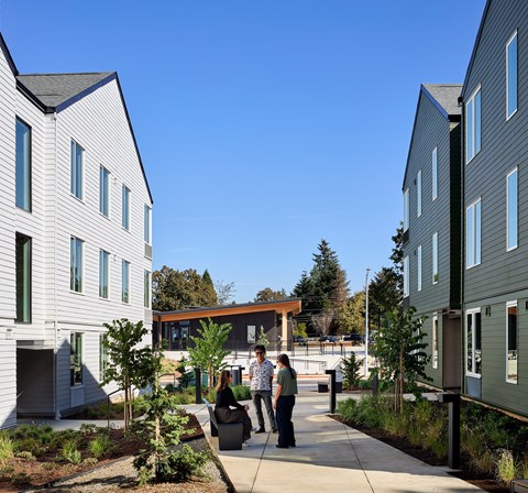 A group of people are walking down a sidewalk between two buildings.