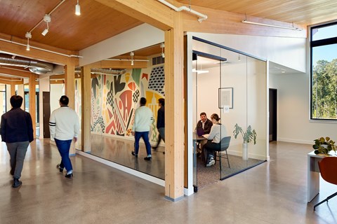 People walking in a hallway with a large painting on the wall.