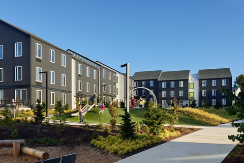 A playground area in front of a building with a slide and a swing set.