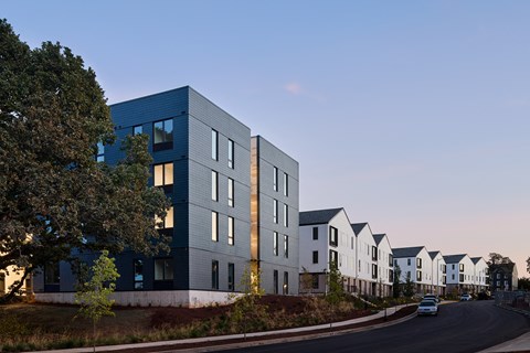A modern building with a blue facade is situated next to a row of white houses.