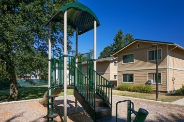 A playground structure with a green canopy and a metal railing is in front of a building.