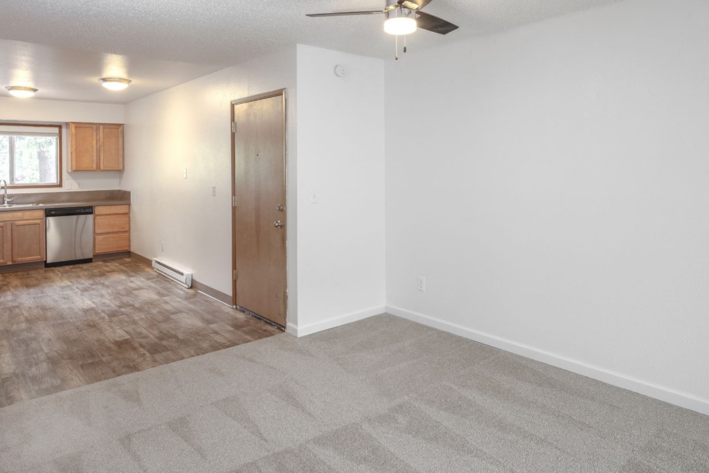 a living room with a ceiling fan and a kitchen in the background