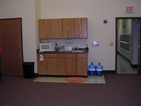 A kitchen area with a microwave, oven, sink and a trash can.