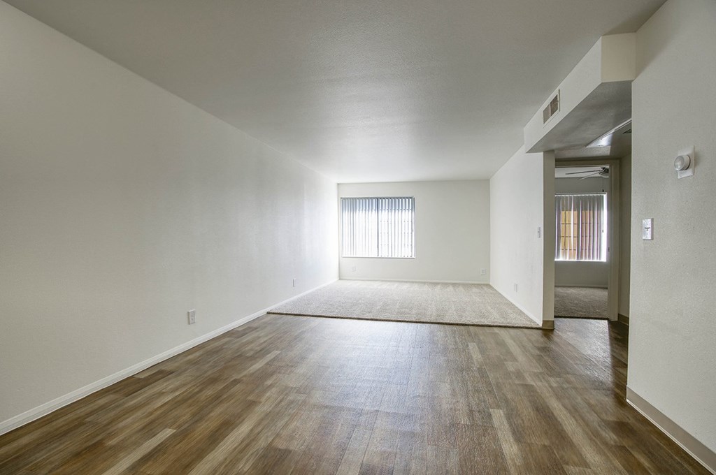 the living room and dining room of an empty apartment with wood floors and white walls