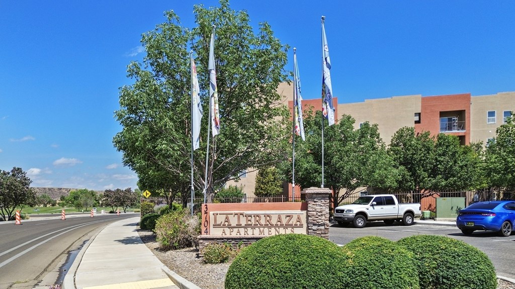 A sign for Laterza Apartments is in front of a building with trees and flags.