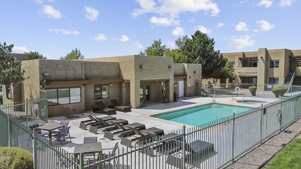 A pool surrounded by a fence and chairs outside a building.