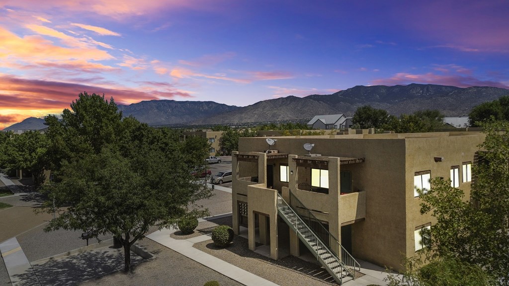 A modern building with a staircase leading to the entrance is surrounded by trees and has a mountain range in the background.