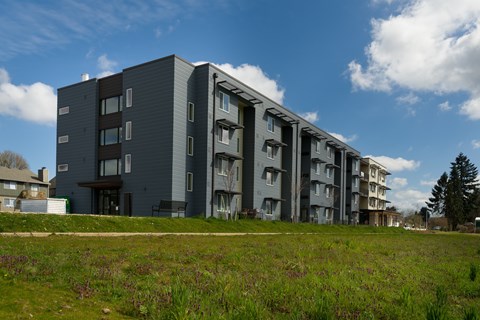 A modern apartment building with multiple balconies and a grassy area in front.