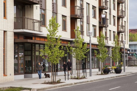A street view of a residential building with people walking on the sidewalk.