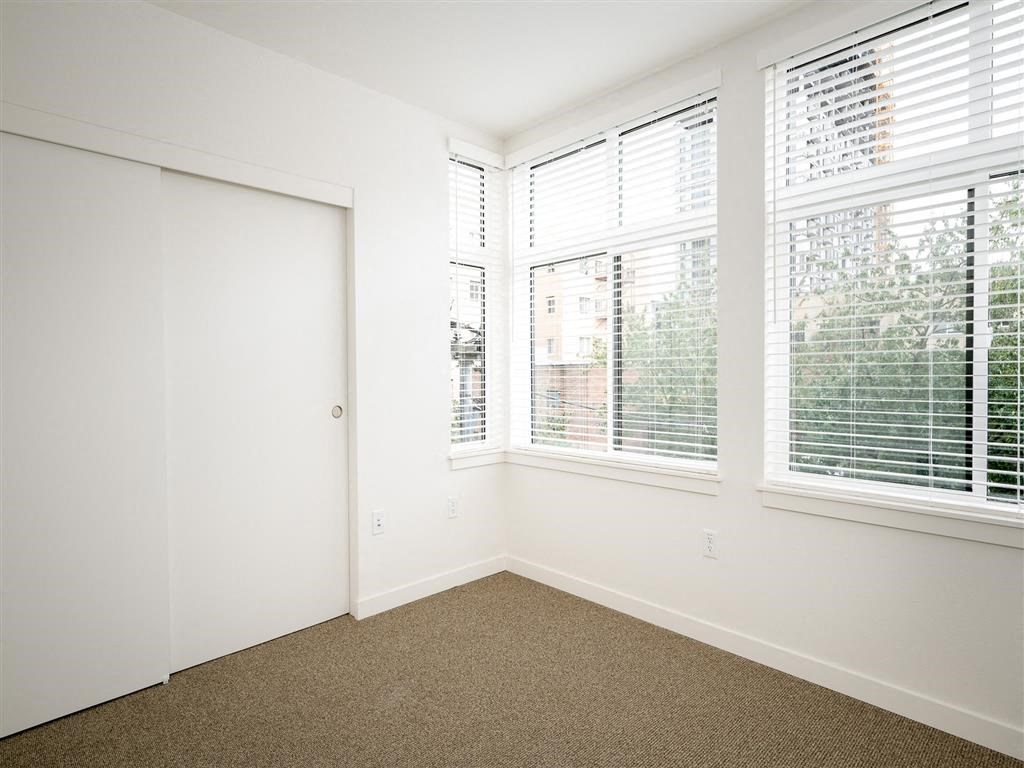 an empty bedroom with three windows and a closet