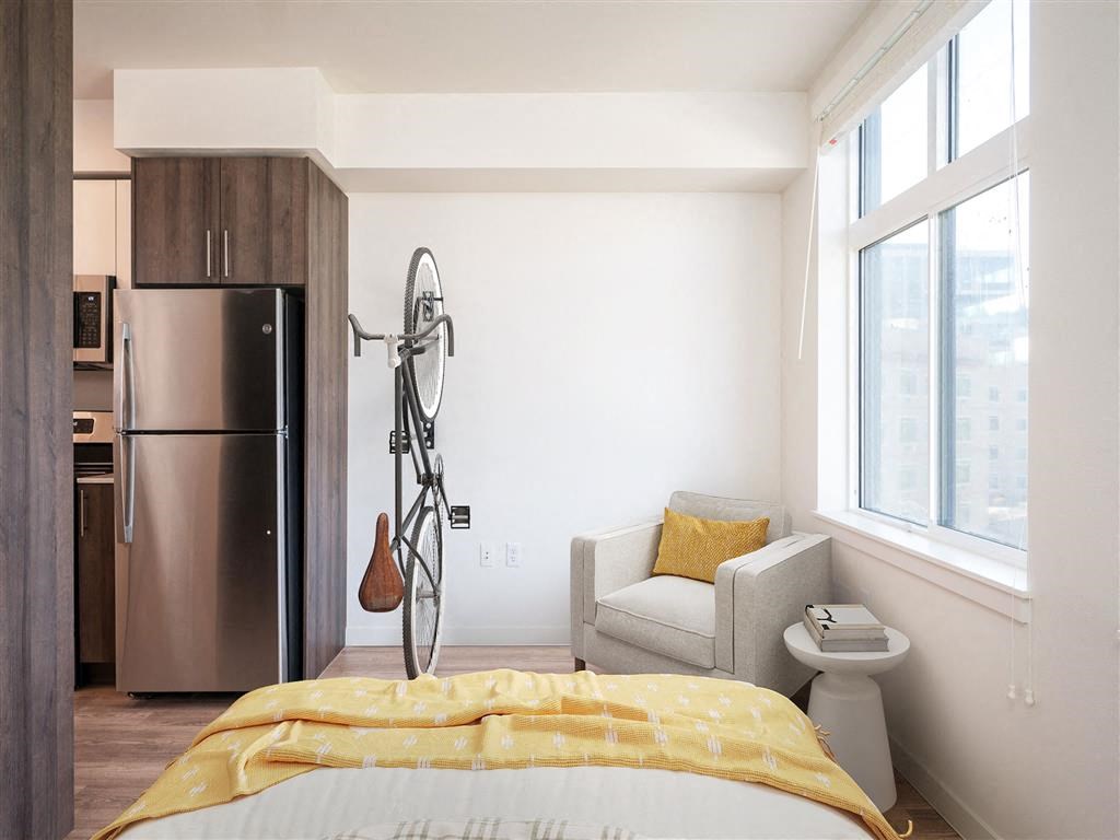 a bedroom with a bed and a refrigerator and a chair and a window