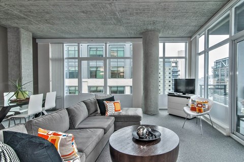 a living room with a gray couch and a tv in a room with large windows