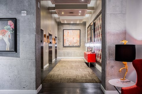 a hallway with a rug and paintings on the wall and a red chair and table