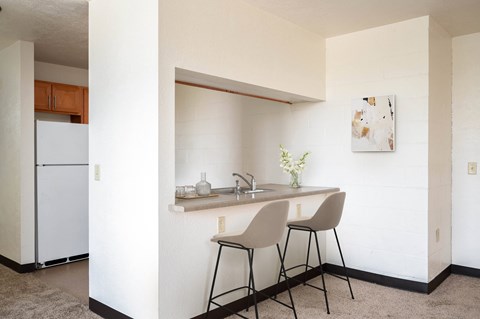A kitchen with a white fridge and a white counter with two chairs.