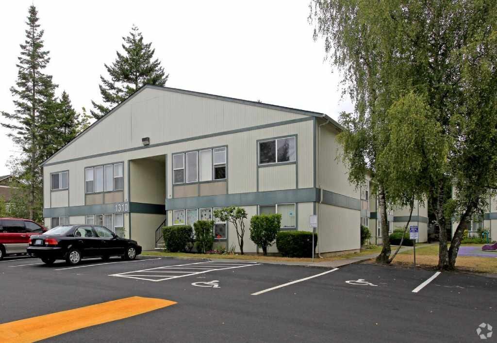 A parking lot in front of a grey building with a black car parked in the spot.