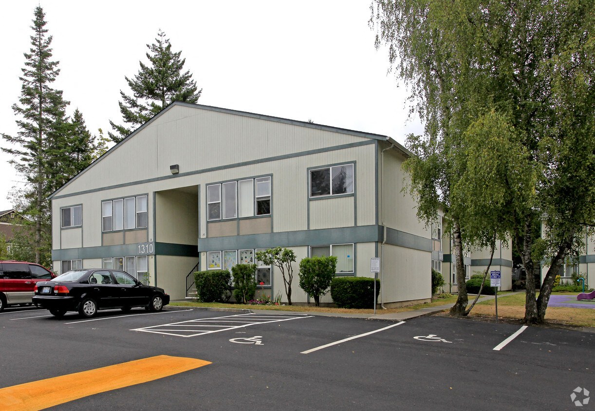 A parking lot in front of a grey building with a black car parked in the spot.