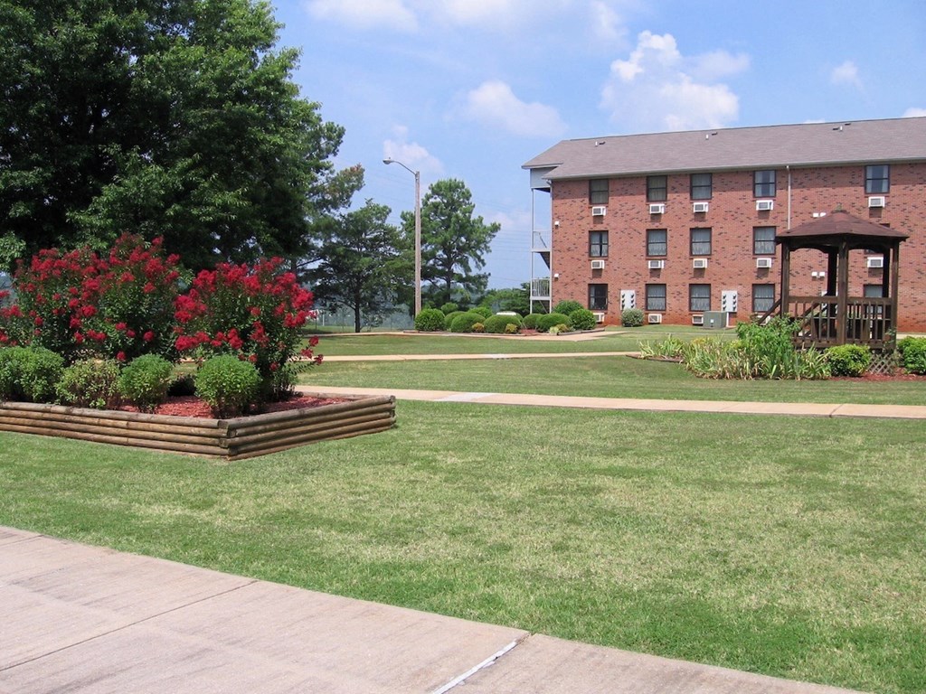 a well-kept lawn with a lush flowwer garden, gazebo, and brick apartment homes at Village Square