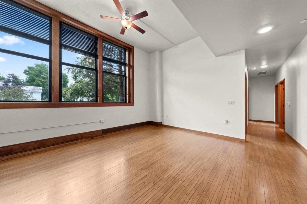 a large living room with a bank of windows on the wall, a ceiling fan, and wood floors