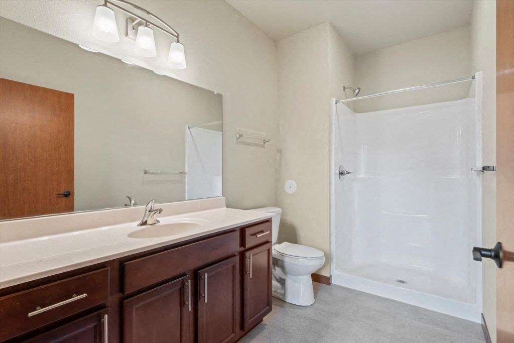 a bathroom with a large sink vanity, mirror, toilet and a shower