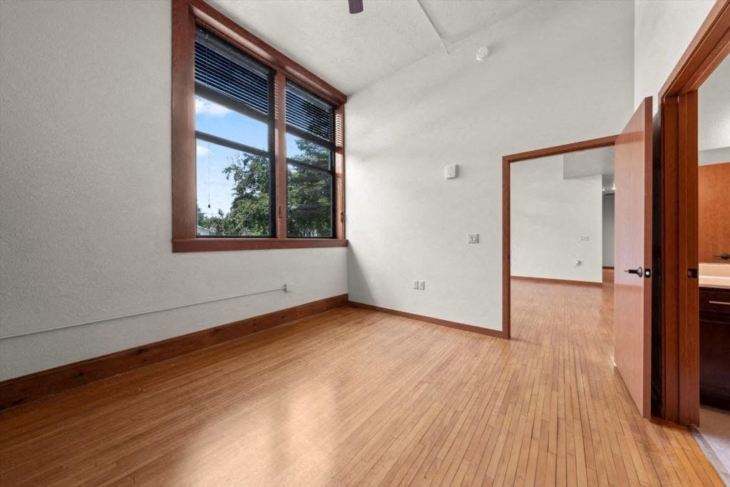 a Spartan Loft room with a large double window, wood flooring, and a high ceiling
