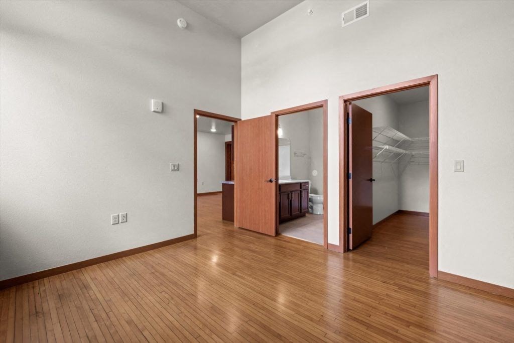 a large bedroom with a walk-in closet, wood-style flooring, and high ceilings in an apartment at Spartan Lofts