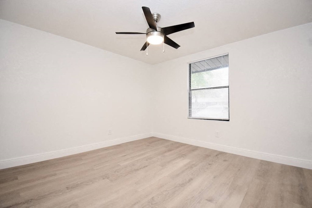 an empty living room with wood-style floors and a ceiling fan
