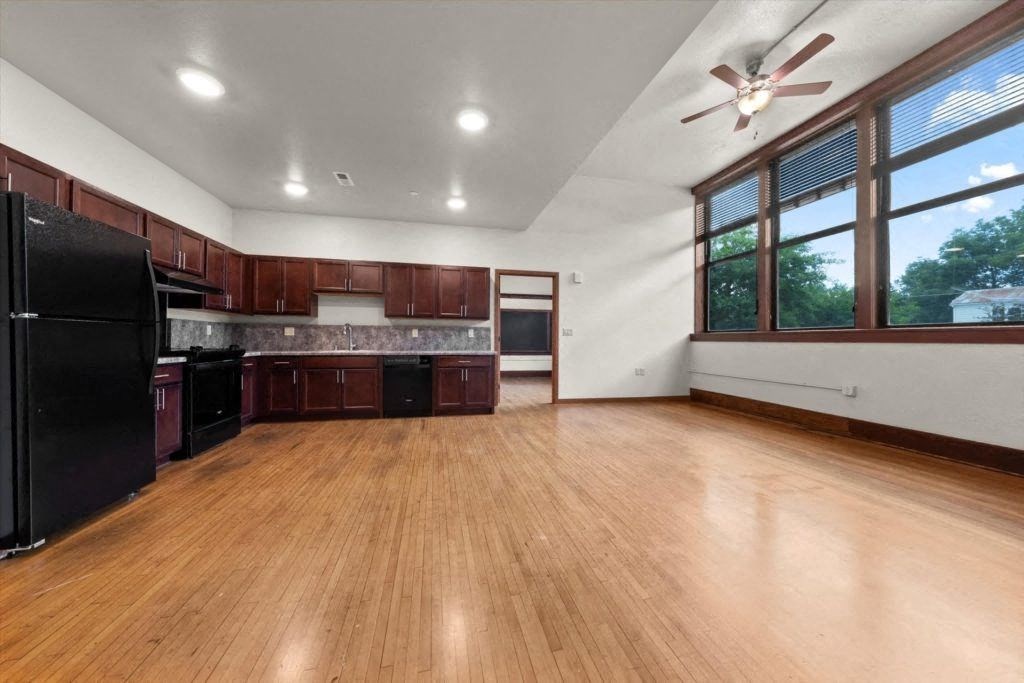a massive kitchen at Spartan Lofts with ample cabinetry, black appliances, wood-floors, large windows, and a ceiling fan