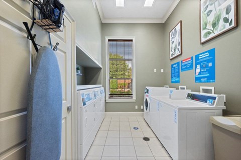 a large laundry center with washers, dryers, and folding tables and an ironing board at Centerville Manor
