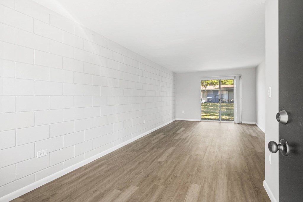 A room with white walls and wooden flooring with a door on the right.