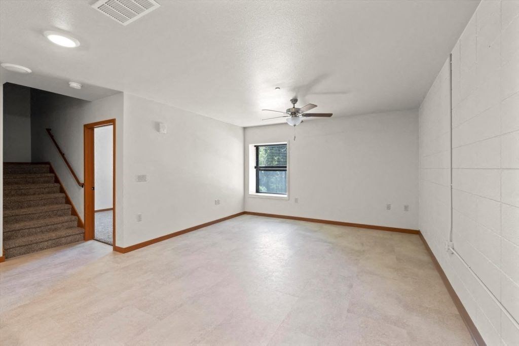 a large downstairs living room with overhead lighting, a ceiling fan, and a window in an affordable Spartan Loft