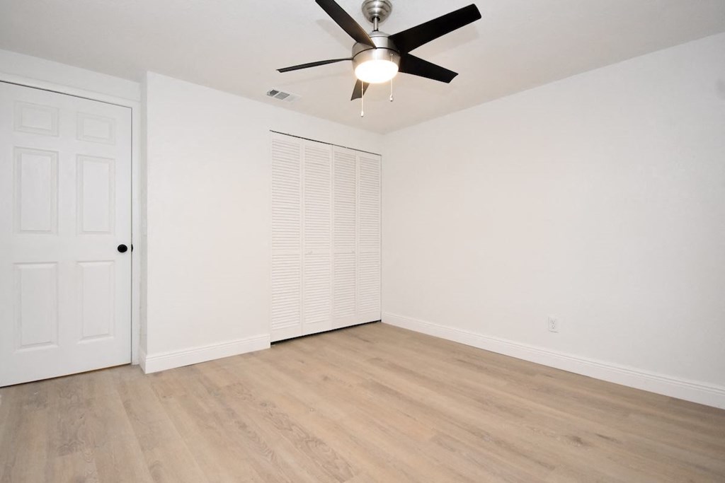 an empty living room with a ceiling fan and a closet