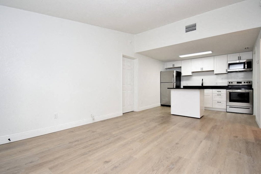 A living room with wood-style flooring and a kitchen with stainless steel appliances