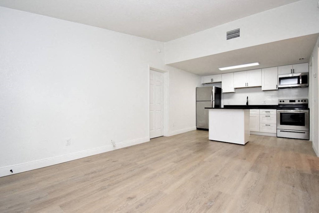 an empty living room and kitchen with white walls and wood-style floors