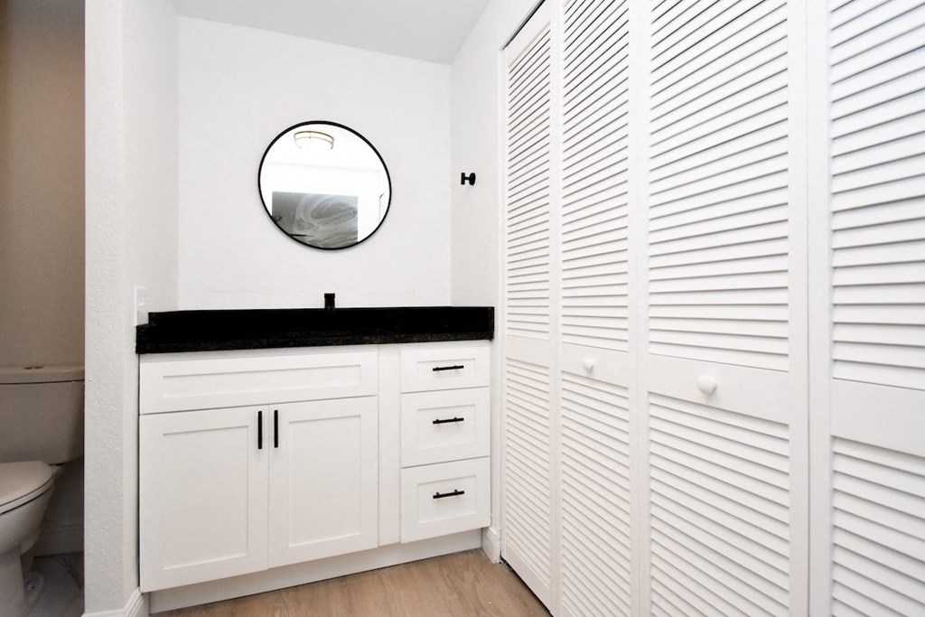 a bathroom with white cabinets, black granite countertop, and a mirror