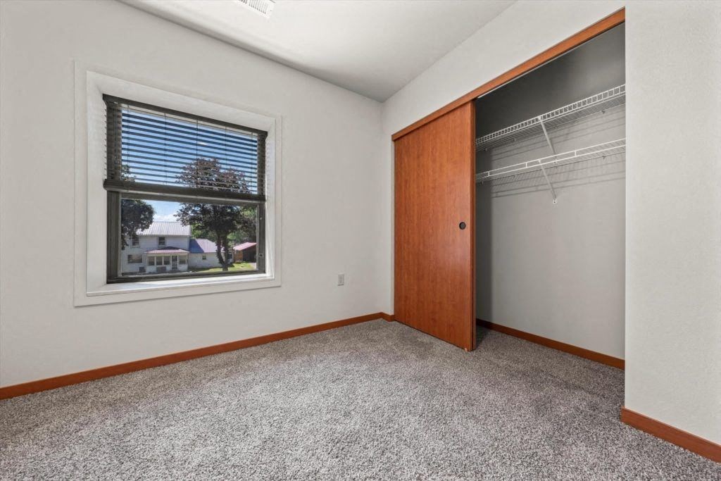 a bedroom with a large window and a double closet at our affordable housing in Sparta, WI