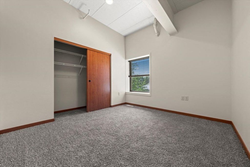 a spacious room with plush carpet, large closet, and window in an affordable home at Spartan Lofts