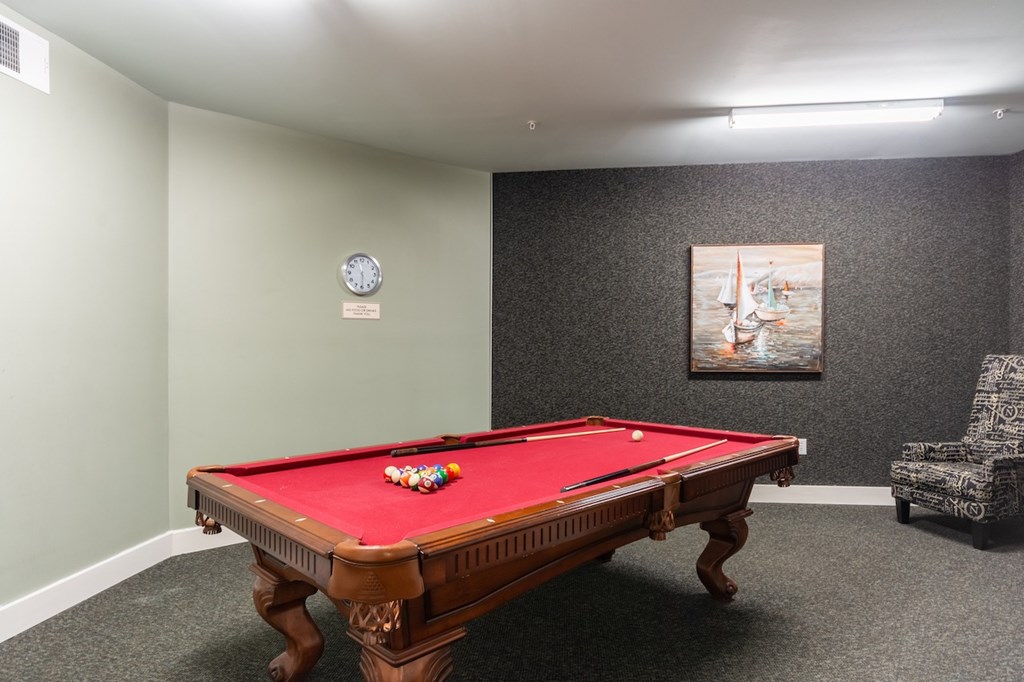 A pool table with a red cloth and a clock on the wall.