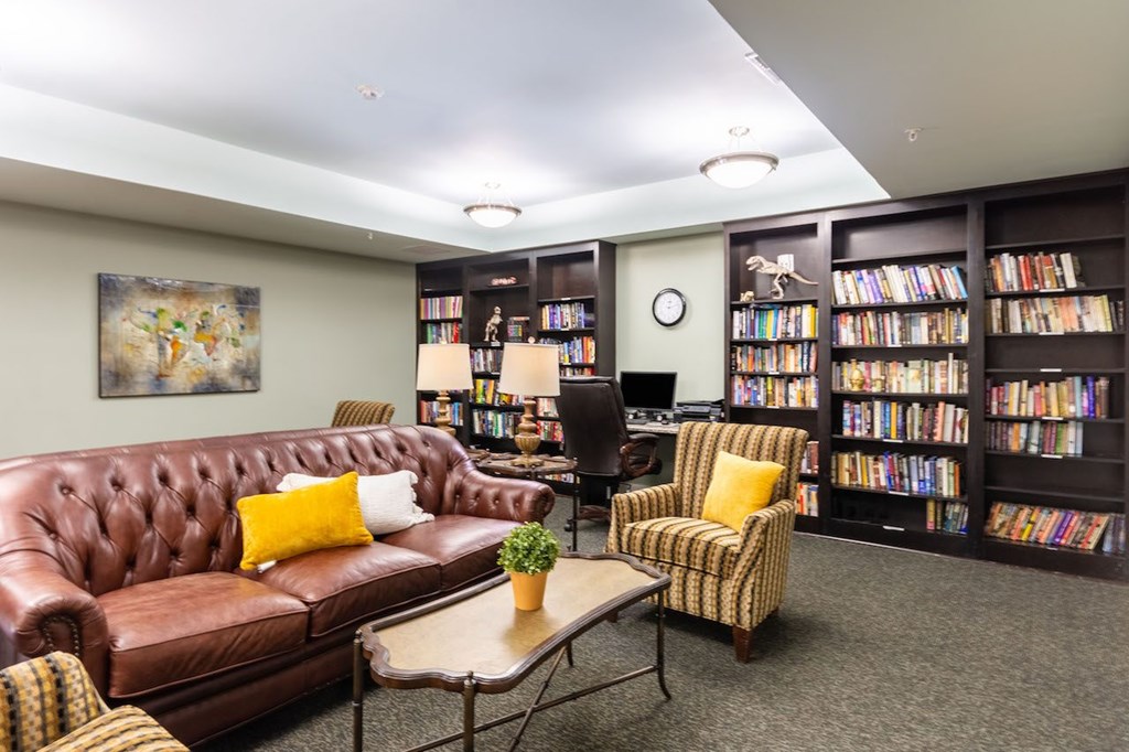 A living room with a brown leather couch, a chair, a coffee table, and a bookshelf filled with books.