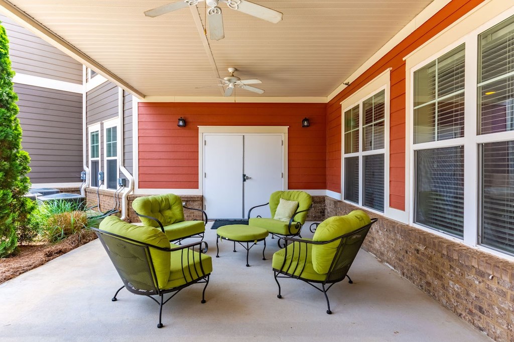 A patio with a white ceiling fan and four green chairs.