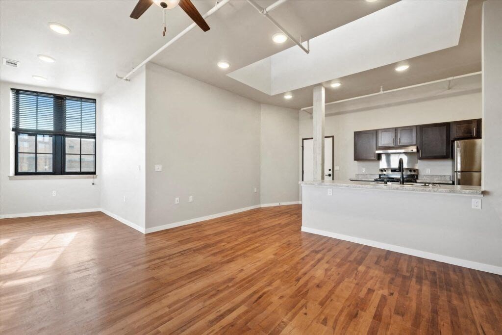 a spacious living room and kitchen with wood floors, ceiling fans, and natural light
