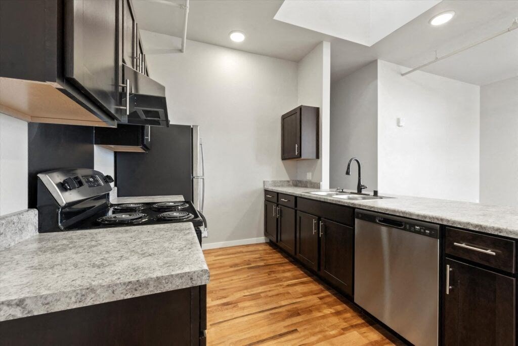 A Brooke Street Lofts kitchen with stainless steel appliances, dark cabinets, and granite-inspired countertops