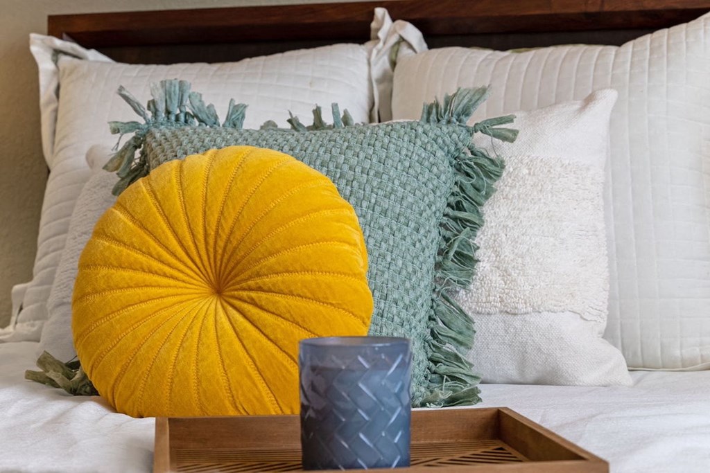 comfortable bed with fluffy white and colored pillows with a tray and candle on a bed