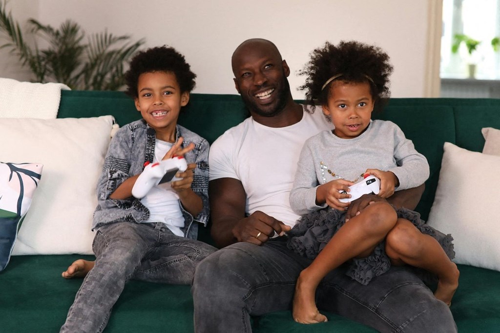 a father and two children sitting on a couch playing video games