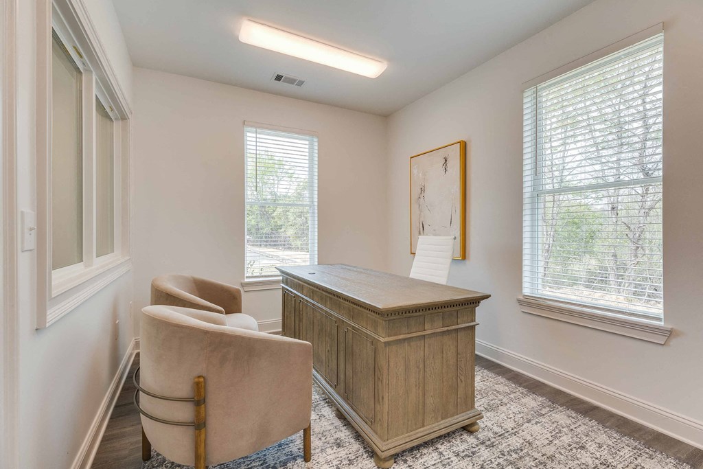 an office with a desk and chairs in a room with two windows