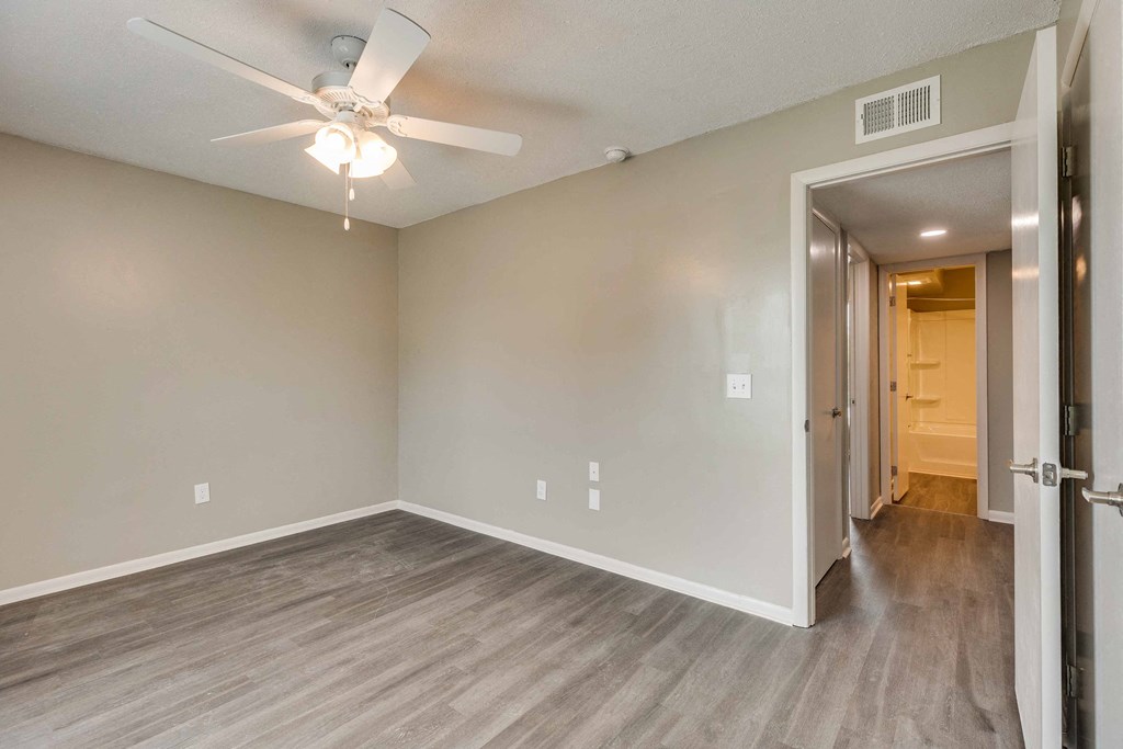 an empty living room with a ceiling fan and a door to a hallway