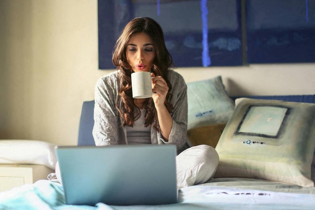 a woman sitting on a bed with a laptop and a cup of coffee