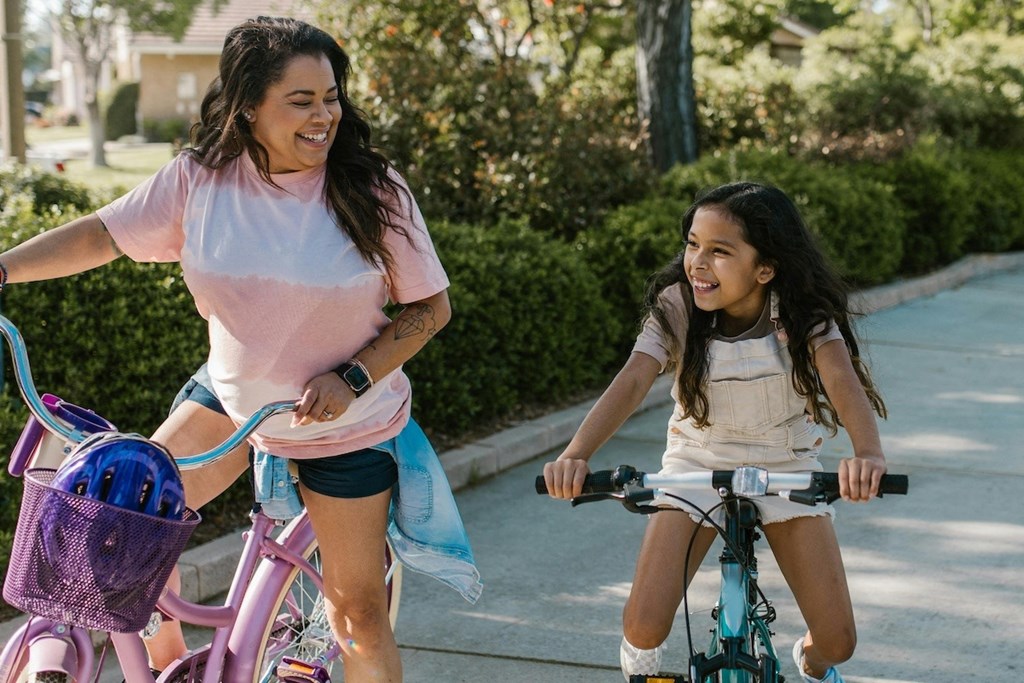a woman and a girl riding bikes on a sidewalk