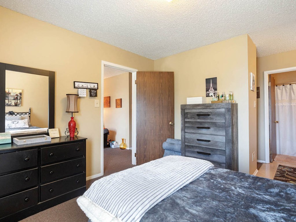 A Village Square Apartment bedroom with a bed and dresser and a closet