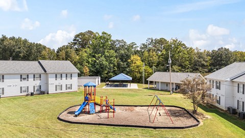 A playground with a blue slide and red swings in the middle of a grassy area.