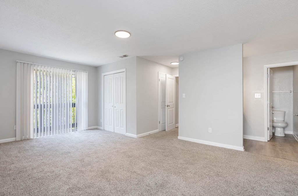 a large carpeted living room with a sliding glass door to the deck and a bathroom with an open door